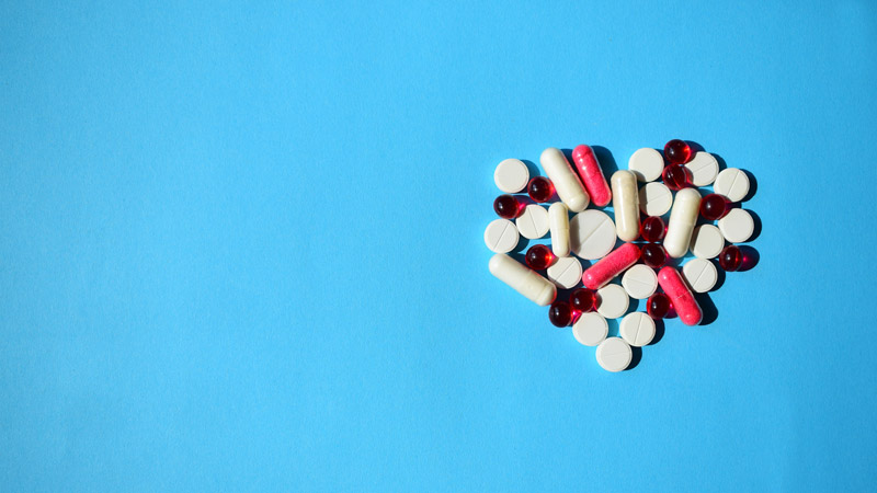 Pile of pills in the shape of a heart on blue background