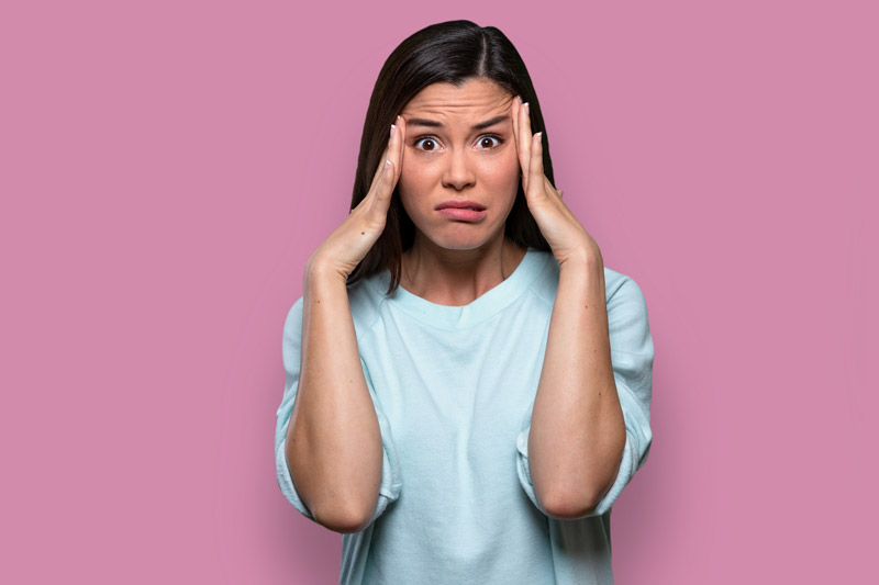 Worried Woman touching her temples on pink background