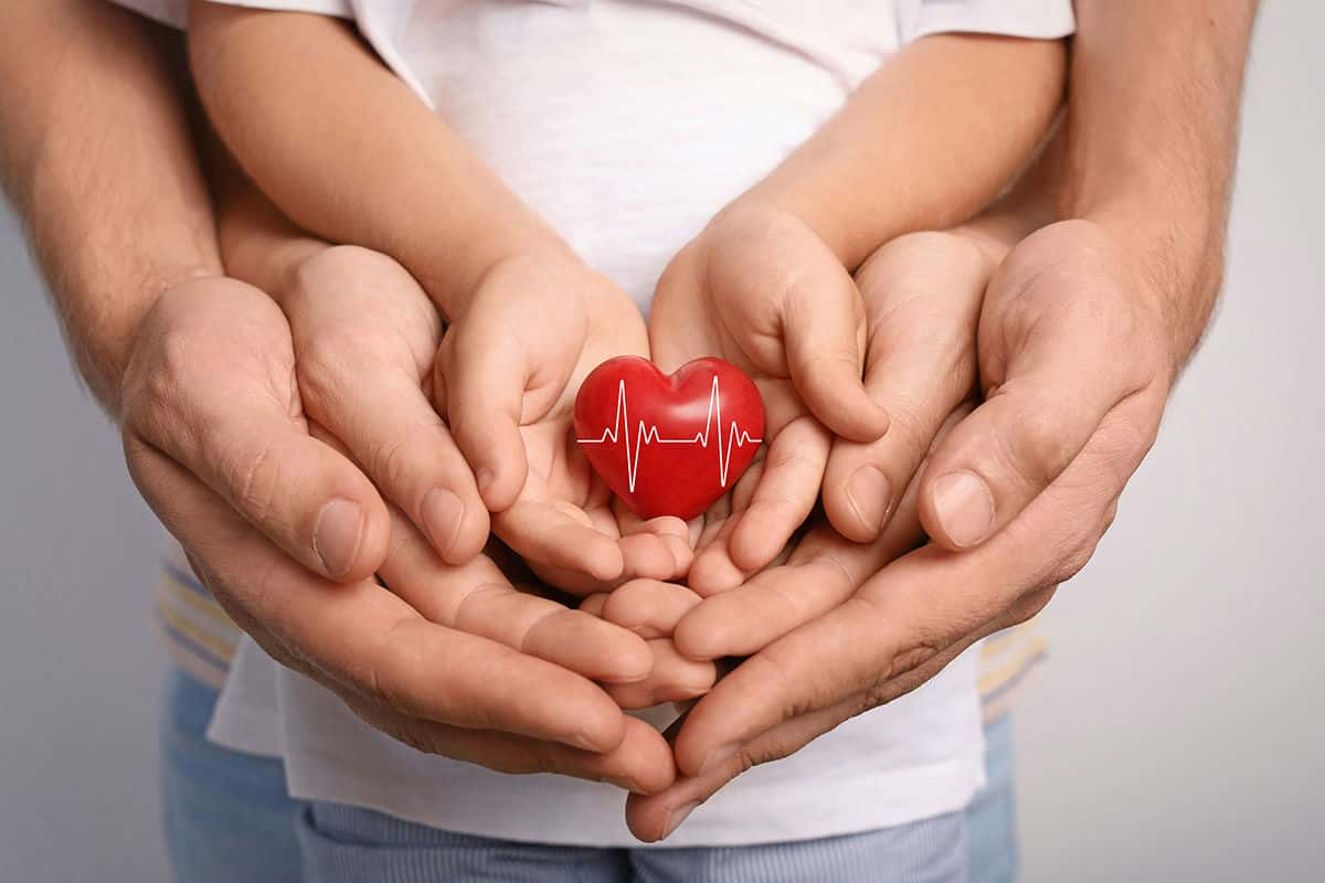 three pairs of hands holding a plastic heart